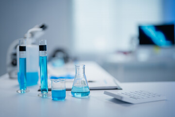 Laboratory setting showcasing various glassware filled with blue liquids. A microscope and computer screen are visible, emphasizing a scientific research environment
