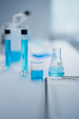 Laboratory scene showcasing blue liquids in various glassware, including beakers and test tubes. A microscope is visible in the background, emphasizing a scientific research setting