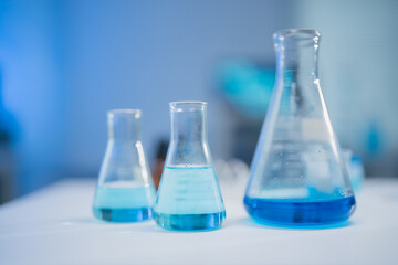 Three laboratory flasks filled with blue liquid, showcasing scientific research and experimentation. The focus is on the varying sizes of the glassware against a blurred laboratory background
