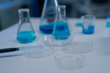 Laboratory setting featuring glassware with blue chemical solutions. Petri dishes and beakers suggest a scientific experiment or research in progress on a clean, white surface