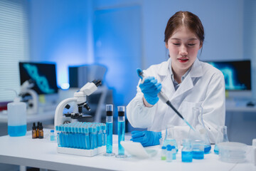 Young scientist in a laboratory using a pipette to transfer blue liquid into test tubes. Advanced research equipment surrounds her, emphasizing a high-tech scientific environment