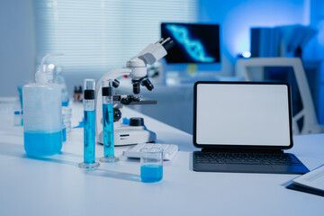 Fototapeta premium Modern laboratory setup featuring a microscope, test tubes with blue liquid, and a tablet. Digital screens display DNA imagery, highlighting scientific research and innovation
