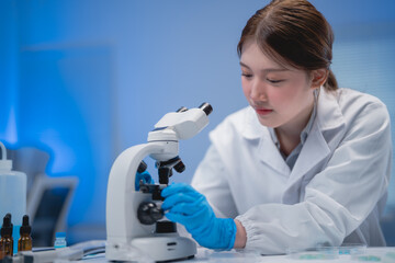 Dedicated scientist in a laboratory setting examines samples using a microscope. Wearing gloves and a lab coat, she focuses on her research in a modern, well-equipped lab