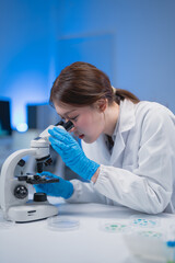 Scientist in a laboratory is closely examining samples under a microscope. Wearing a lab coat and...