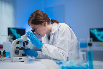 Focused scientist wearing gloves examines samples under a microscope in a modern laboratory. Blue...