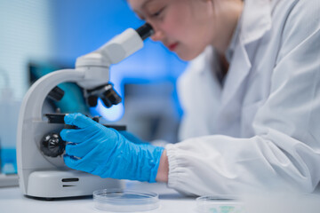 Scientist in a lab coat and gloves examines a sample under a microscope in a laboratory setting....
