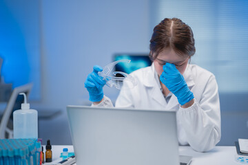 Young scientist removing protective glasses and rubbing her tired eyes, feeling overwhelmed after a...