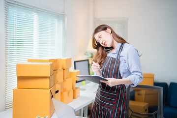 Young entrepreneur managing her online business, talking on the phone with customers and taking...