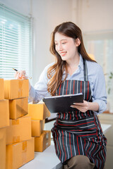 Young asian woman entrepreneur, small business owner checking cardboard boxes and writing notes on a clipboard while working at home office, online marketing packaging and delivery concept