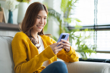 Happy young asian use phone texting messaging on smartphone,chatting online message,online shopping on comfortable couch at home.Smiling asian girl relax time use cellphone,shopping online from home