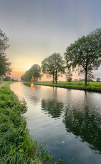 A calm river captures the beauty of a stunning sunset, framed by lush green trees in a serene atmosphere
