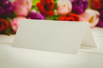 Flat design blank tent-folded card is sitting on wooden tabletop with blurred tulip blooms behind