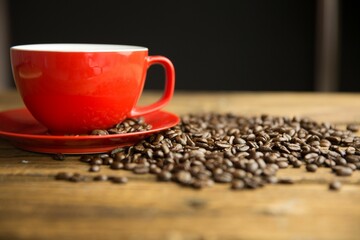 Flat design showing red coffee cup resting on wood table with scattered beans against dark backdrop