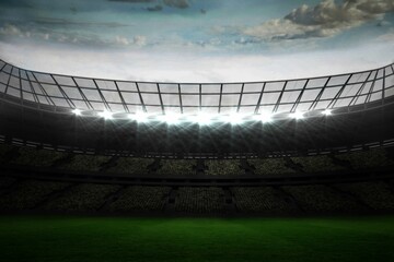 Empty stadium showing seating beneath metal roof, floodlighting green field under partly cloudy sky