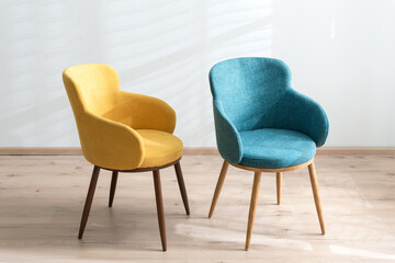 Minimalist interior with two modern accent chairs, one mustard yellow and one teal blue, both...