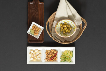 Top view of assorted snacks including green olives in ceramic bowl, cheese cubes, roasted peanuts,...