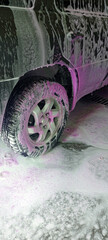Car wash close-up with white and vibrant pink foam covering the vehicle. Self-service station. Cleaning process. Perfect for auto care, maintenance, and service concepts. Advertising.