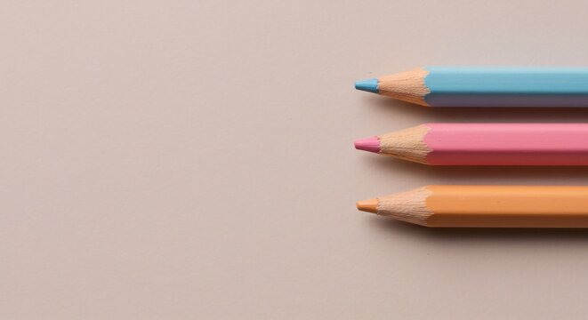 Three pastel colored pencils arranged neatly on a beige background with copy space