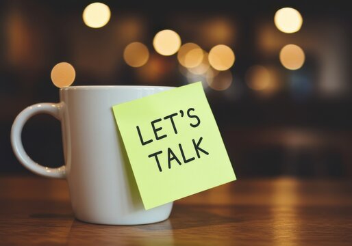 A white coffee mug with a bright yellow sticky note saying let s talk