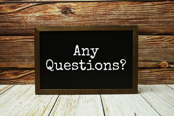 Any Questions? text written on chalkboard standing on wooden background