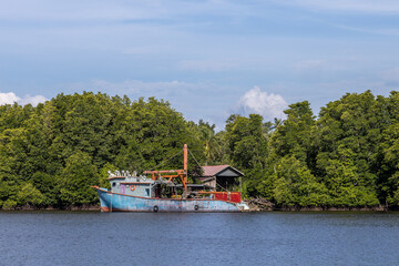 A traditional fishing boat is moored near a wooden house by the mangrove forest in Kuala Penyu,...