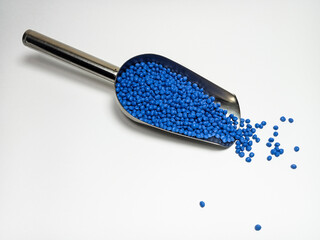 Blue plastic masterbatch, polymer carries colorful pigments with small scoops poured into a white background, suitable for product catalog design of industrial plastic manufacturing company profiles