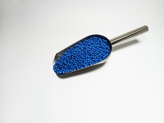 Blue plastic masterbatch, polymer carries colorful pigments with small scoops poured into a white background, suitable for product catalog design of industrial plastic manufacturing company profiles