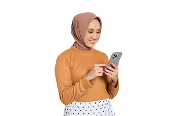 Cheerful young Muslim woman in hijab texting on smartphone while standing isolated on transparent background