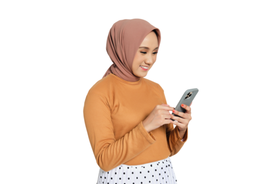 Cheerful young Muslim woman in hijab texting on smartphone while standing isolated on transparent background