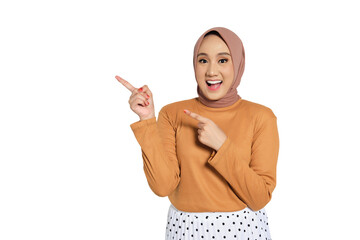 Excited Muslim woman in hijab smiling widely and pointing up with enthusiastic expression isolated...