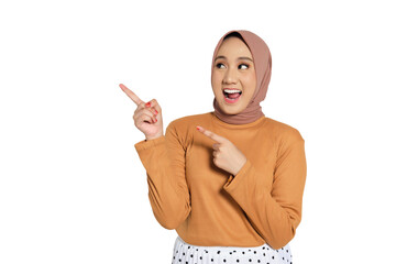 Excited Muslim woman in hijab smiling widely and pointing up with enthusiastic expression isolated...
