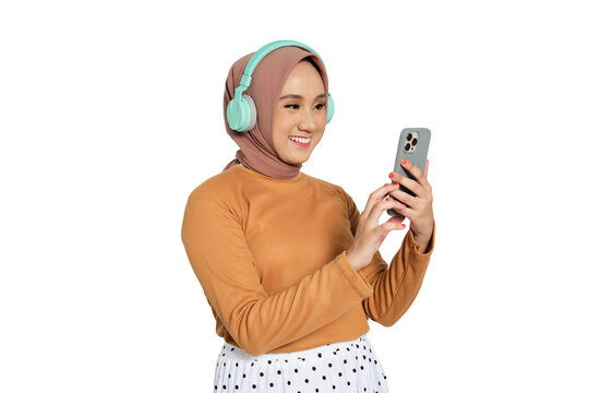 Muslim woman in hijab wearing headphones and using smartphone while smiling isolated on transparent background