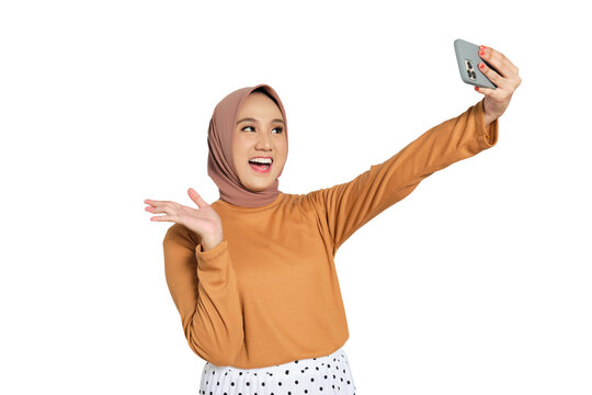 Cheerful Muslim woman in hijab taking selfie with smartphone and waving hand isolated on transparent background - Powered by Adobe