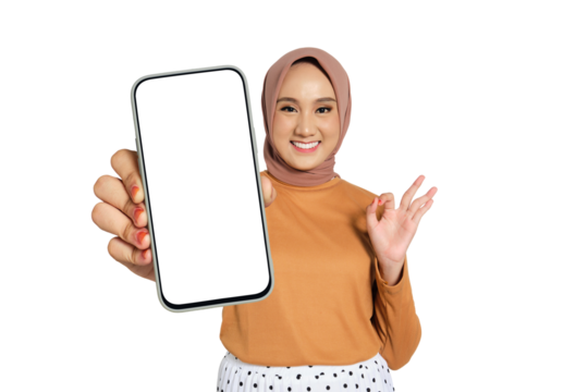 Smiling woman wearing hijab showing blank smartphone screen and making OK gesture isolated on transparent background