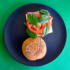 A cold Danish salami burger with cheese, tomato and spinach leaves on a brioche bun with seeds. 