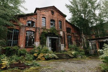 Obraz premium Abandoned brick factory with broken windows and dense overgrown plants in a dark setting