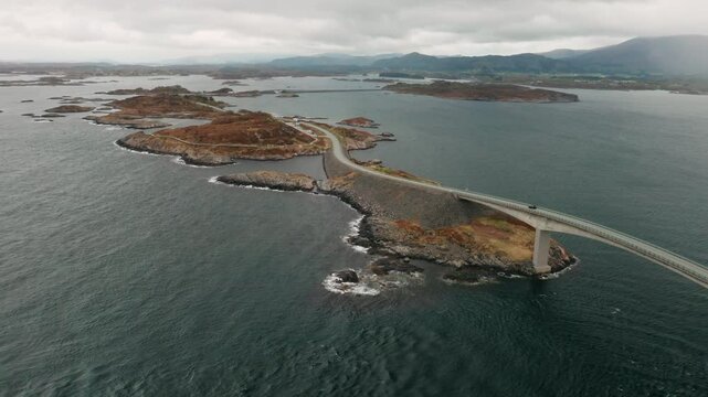 Atlantic ocean road displays rugged terrain meeting small islands. Road gracefully curves over water demonstrating remarkable engineering in Norway