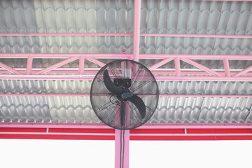 A black fan is mounted on a steel pole painted pink.