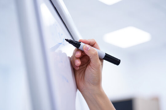 Hand holding a black marker writing on a white board in a bright environment