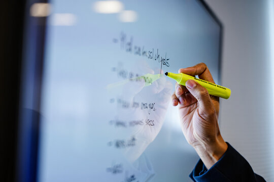 A hand writing on a whiteboard with a yellow marker in a conference room area
