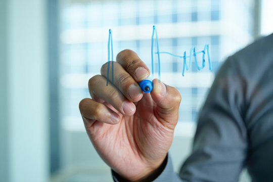 Man drawing a chart on a glass board with a blue marker in a bright office
