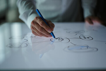 A person drawing a diagram on a white surface with a blue pen in their hand