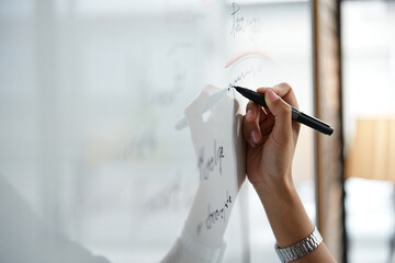 A person writing on a whiteboard with a black marker in a bright environment