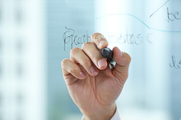 A hand writing on a transparent board with a black marker in a bright room