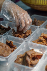 A hand wearing a transparent plastic glove put golden brown, crispy beef pieces in clear plastic...