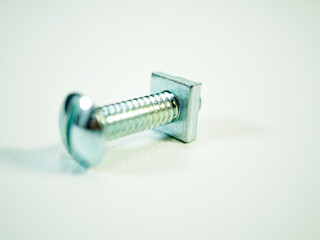 Shiny metal screw with square nut gleams on a clean white surface, a small fastener for building...
