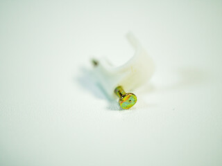 Close up on a cable clip with a nail on a white textured surface for tidy wire management and...