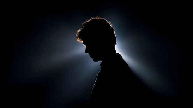 Silent Contemplation: A silhouette of a person in deep thought, illuminated by a single ray of light, captures a moment of introspection and quiet contemplation in a dark, atmospheric setting.