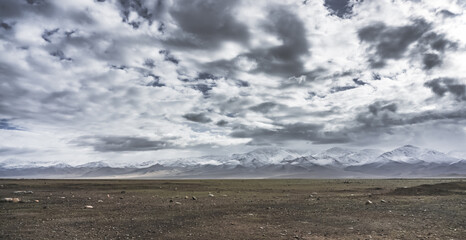 Dramatic landscape panorama of mountain peaks with snow and glaciers in cloudy weather, rays of the sun breaking through the clouds, landscape of the Pamir mountains for the background