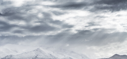 Dramatic landscape panorama of mountain peaks with snow and glaciers in cloudy weather, rays of the sun breaking through the clouds, landscape of the Pamir mountains for the background